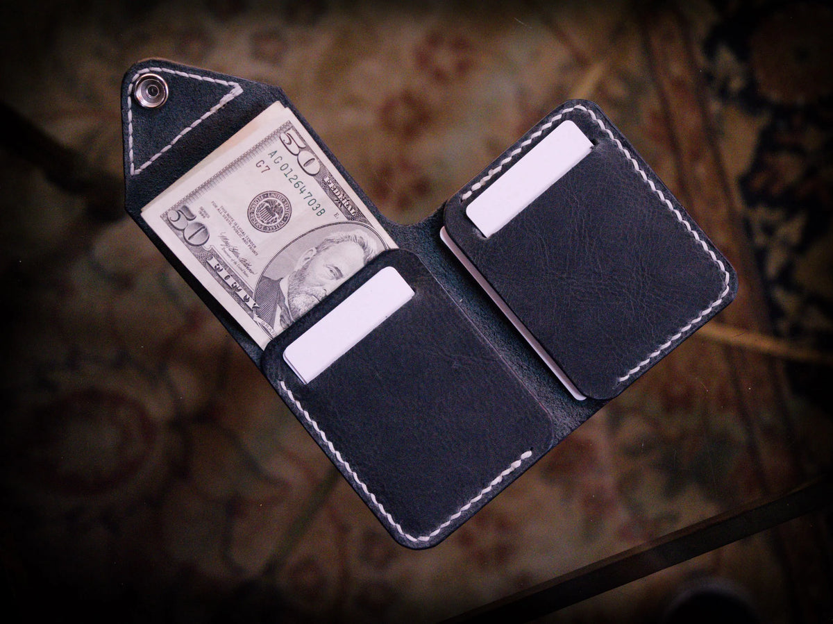 Handmade black chrome-tanned leather snap wallet, open showing three card pockets and cash pocket Black leather snap wallet with white saddle stitching, handmade in America Handmade snap wallet closed, black chrome-tanned leather with snap rivet closure
