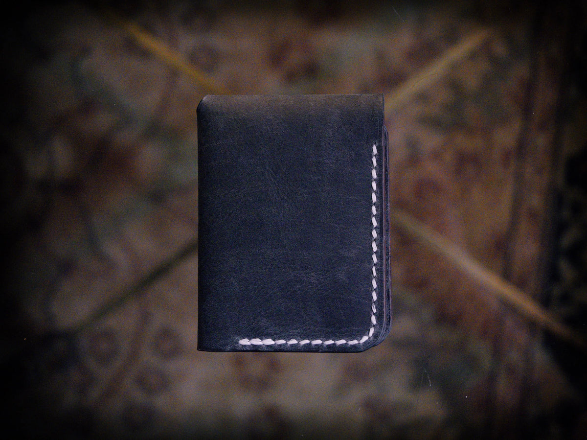 Handmade black chrome-tanned leather snap wallet, open showing three card pockets and cash pocket Black leather snap wallet with white saddle stitching, handmade in America Handmade snap wallet closed, black chrome-tanned leather with snap rivet closure
