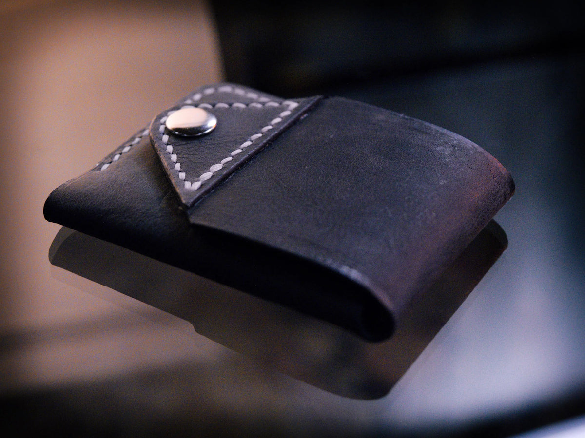 Handmade black chrome-tanned leather snap wallet, open showing three card pockets and cash pocket Black leather snap wallet with white saddle stitching, handmade in America Handmade snap wallet closed, black chrome-tanned leather with snap rivet closure
