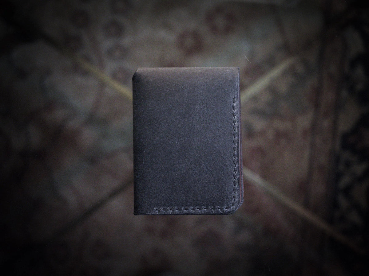 Handmade black chrome-tanned leather snap wallet, open showing three card pockets and cash pocket Black leather snap wallet with white saddle stitching, handmade in America Handmade snap wallet closed, black chrome-tanned leather with snap rivet closure
