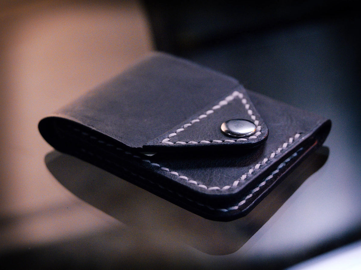 Handmade black chrome-tanned leather snap wallet, open showing three card pockets and cash pocket Black leather snap wallet with white saddle stitching, handmade in America Handmade snap wallet closed, black chrome-tanned leather with snap rivet closure
