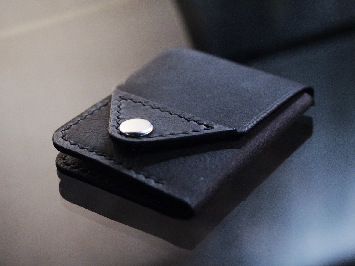 Handmade black chrome-tanned leather snap wallet, open showing three card pockets and cash pocket Black leather snap wallet with white saddle stitching, handmade in America Handmade snap wallet closed, black chrome-tanned leather with snap rivet closure
