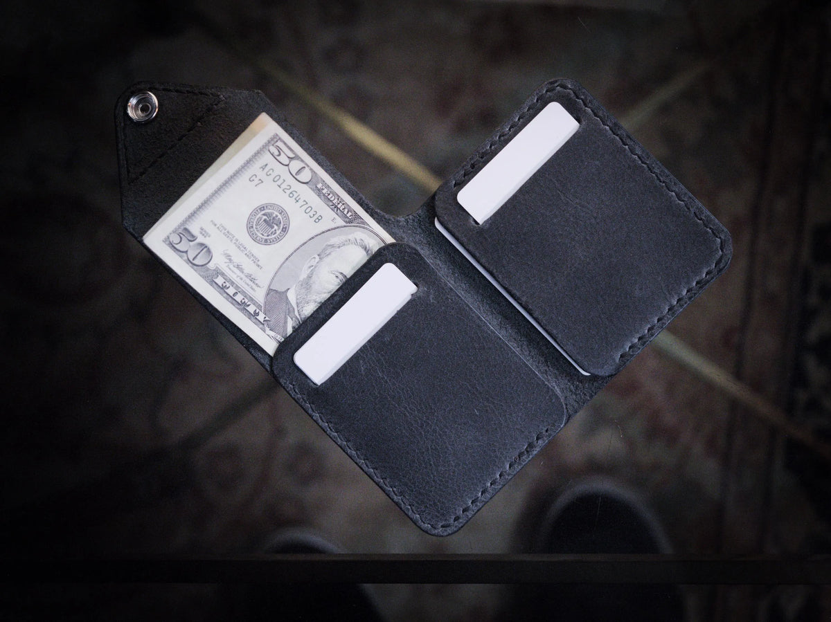 Handmade black chrome-tanned leather snap wallet, open showing three card pockets and cash pocket Black leather snap wallet with white saddle stitching, handmade in America Handmade snap wallet closed, black chrome-tanned leather with snap rivet closure
